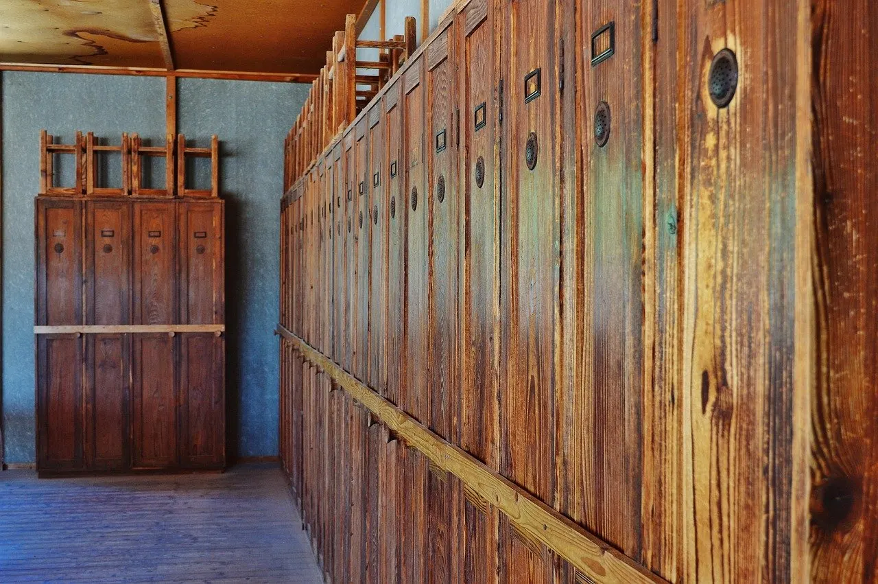 Lange Reihe alter Holzschränke mit Messingbeschlägen und Ziernieten in einem Flur, Holz wirkt vergilbt und verwittert.