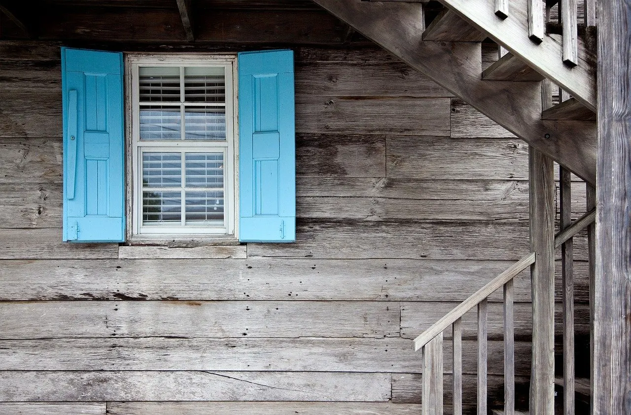 Blau lackierte Fensterläden an einem Holzhaus mit Fenster und Treppe