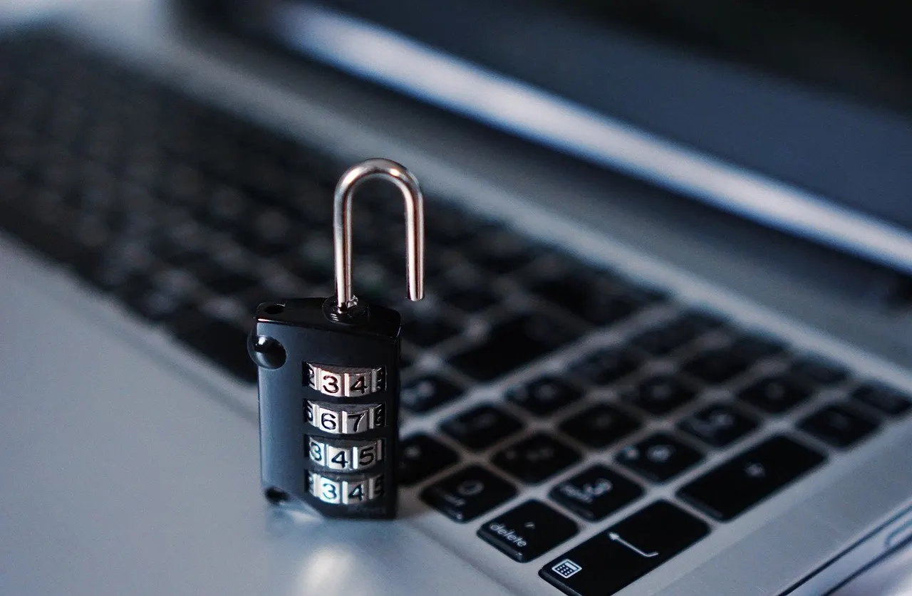 Offenes Zahlenschloss mit vier Ziffernrollen steht auf einer Laptoptastatur.